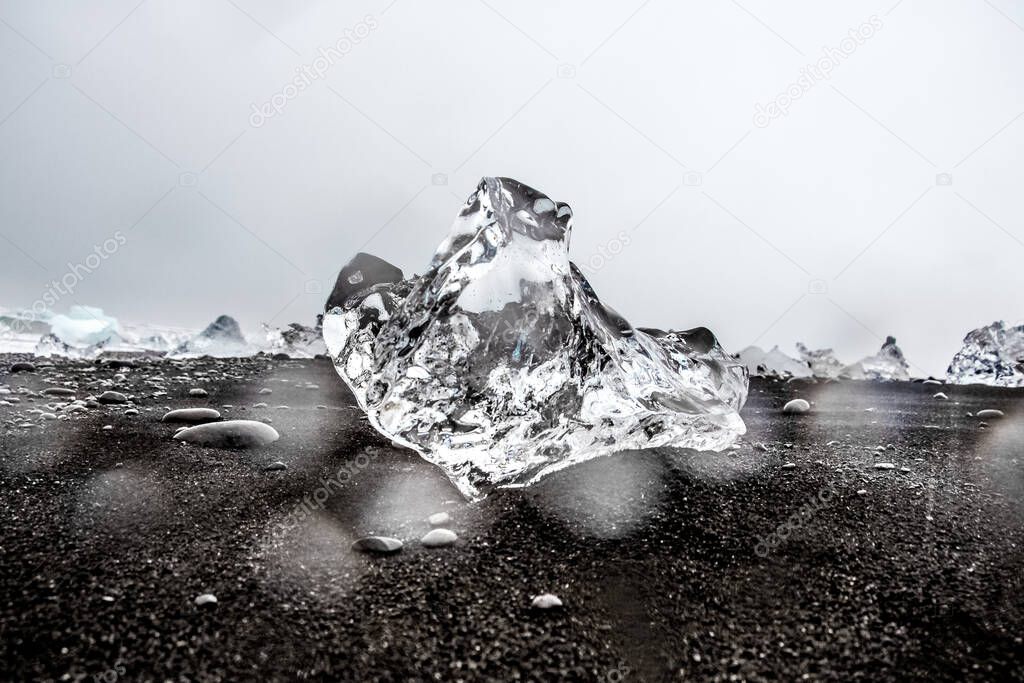a piece of transparent ice on black volcanic sand, black beach, a trip to Iceland. High quality photo