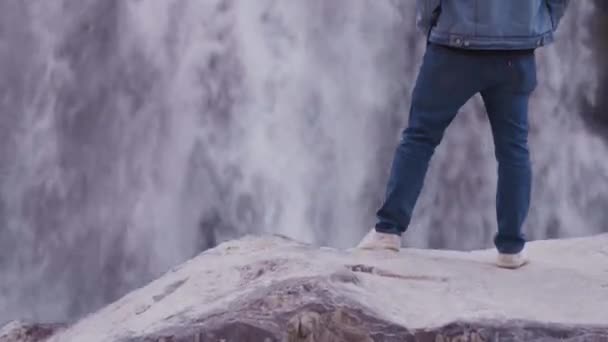 Молодий Індіанець Стоїть Скелі Впевнено Дивиться Водоспад Одягнувши Синій Джинсовий — стокове відео