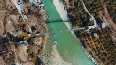 Hindistan 'ın Uttarkashi eyaletinin Harsil, Uttarkashi ilçesinde elma bahçeleri, sarı ağaçlar, evler ve dağlarla çevrili Bhagirathi nehri üzerindeki köprü manzarası.