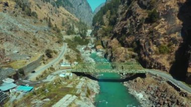 Güzel Bhagirathi nehri, Uttarakhand, Hindistan 'ın Uttarkashi ilçesindeki devasa kahverengi dağlar ve yeşil ağaçlarla çevrili Highway yolu kıyısındaki köprünün altından taşların arasından akıyor..