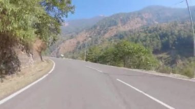 Empty long mountain rural road of National Highway 34 connecting Uttarkashi - Gangotri Road on the way to Harsil. POV of car driving on highway road Surrounded by forests.