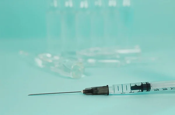 a disposable syringe with a long needle lies against the background of ampoules. a vaccine-filled syringe.a medical instrument for administration.