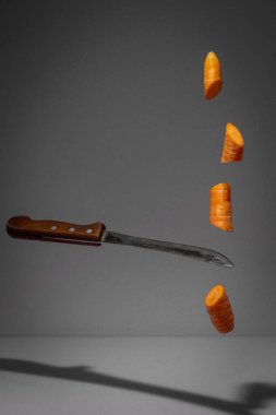 Havuç doğrayan yüzen bıçak. Gri arka plan. Yaratıcı gıda konsepti