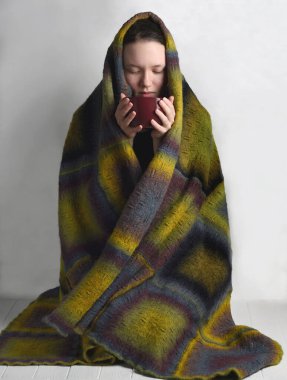 El yapımı merino yün battaniyeyle kaplı genç bir kız elinde hafif arka planda sıcak içecekle bir bardak tutuyor. Sıcak kış konsepti.