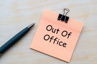 Out Of Office, Pink notepad with metal clip and pen beside it on wooden table representing workplace break announcement