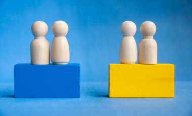 Ahşap figürler mavi ve sarı bloklarda gruplandırılmış sosyal bölünmeyi, liderlik hiyerarşisini ve fırsat boşluklarını sembolize ediyor.