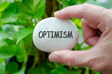 Üzerinde iyimser bir yazı işlenmiş beyaz bir taşı tutan el, umut ve olumlu bakış açısının yaşam amacını yansıtıyor.