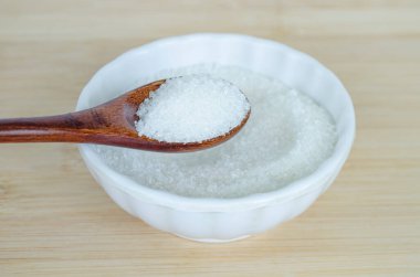 Beyaz kasenin içinde dinlenen ahşap kaşığa tuz koy baharat bileşenini vurgula ve sağlıklı yaşam tarzı seçimleri için sodyum tüketimini kontrol et.