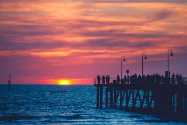 İnsanlar gün batımında Glenelg Jetty 'de geziniyorlar, Güney Avustralya
