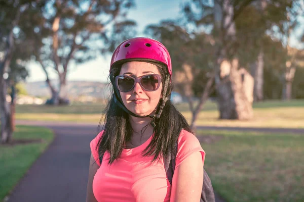 日落时分骑自行车穿越阿德莱德公园时戴着粉色上衣和自行车头盔的年轻女子的自然画像 — 图库照片