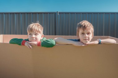 Küçük çocuklar arka bahçede büyük bir kutunun içinde oturuyorlar.