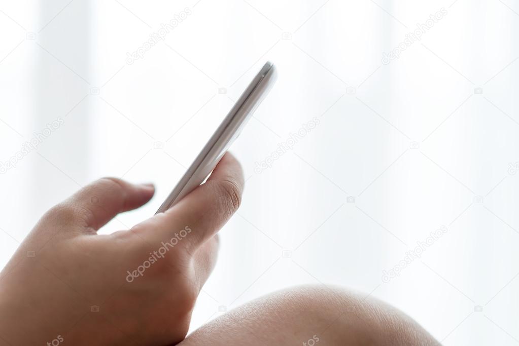Woman holding mobile phone in front of the window
