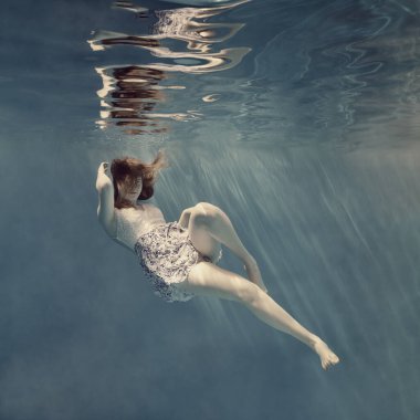 Sıfır yerçekimi, açık mavi arka plan ve su yüzeyinde güzel bir yansıma gibi su altında elbise giymiş bir kız.