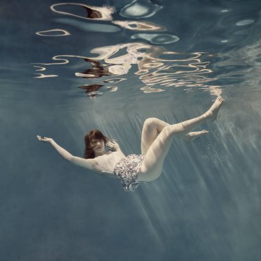 Sıfır yerçekimi, açık mavi arka plan ve su yüzeyinde güzel bir yansıma gibi su altında elbise giymiş bir kız.