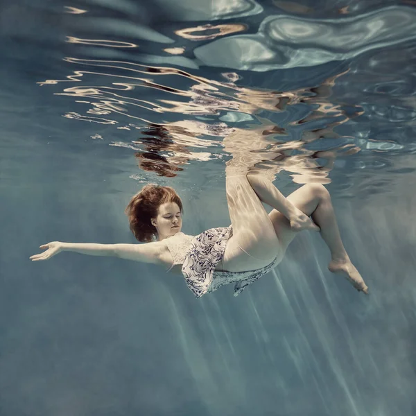 在水下穿礼服的女孩 好像没有重力 浅蓝色背景 水面上有美丽的倒影 — 图库照片