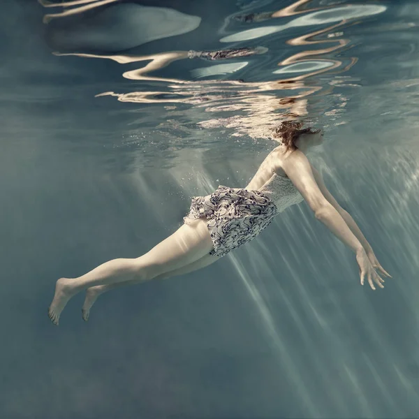 在水下穿礼服的女孩 好像没有重力 浅蓝色背景 水面上有美丽的倒影 — 图库照片