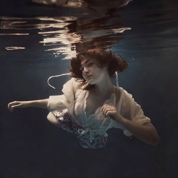 나부끼는 소녀는 어두운 배경에 무중력 상태로 떠다니는 것처럼 물속을 헤엄친다 — 스톡 사진