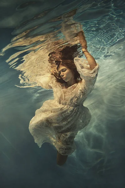 A girl in a white lace dress swims underwater as if flying in zero gravity