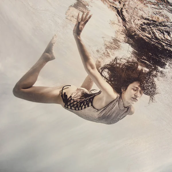 一个穿着银色西服的女孩在浅浅的背景下在水里游泳 好像在飞翔 — 图库照片