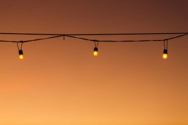 Eski tip ampuller, günbatımı dekoruna karşı tel üzerinde.