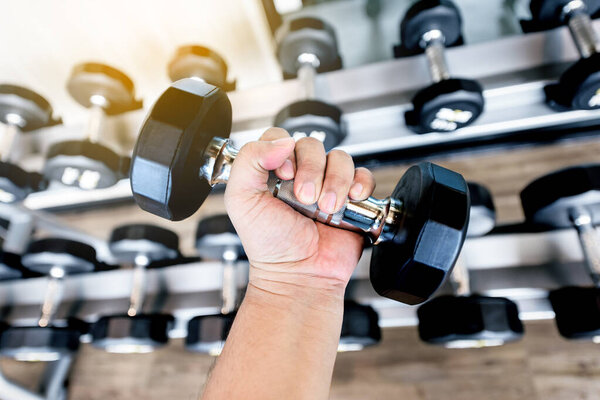 fat man Hand holding  black metal dumbbells in the gym 