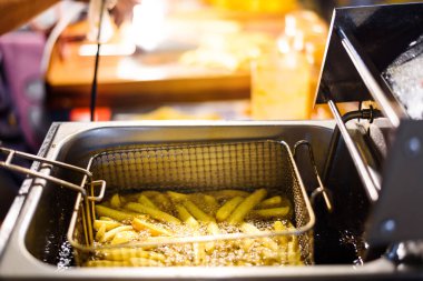 Kızartma makinesinde patates kızartması pişirme sepetini kapat, kızgın yağda kızart.