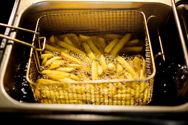 close up French Fries Potatoes cooking in basket of Frying Machine , deep fried in Hot Boiling Oil