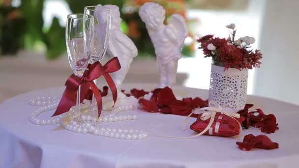 Bröllop glas på bordet i bakgrunden två vita änglar, pärlor och ökade blomblad. — Stockvideo