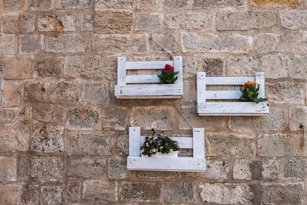 Taş duvarda çiçekler olan ahşap raflar..
