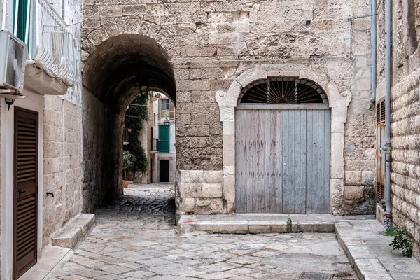 Small courtyard, arched passage, stone walls, closed doors. Monopoli, Italy.