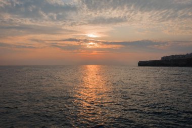 Bulutlarda gün doğumu. Deniz suyundaki altın yol. Polignano, İtalya.