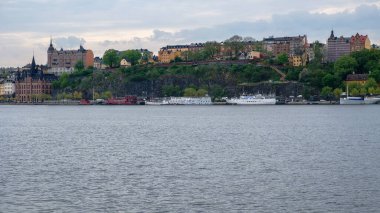 Yüksek bir kıyıdaki şehir binaları. Rıhtımda nehir gemileri var. Yaz Stockholm, İsveç.