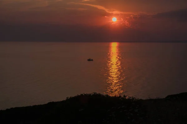 Sonsuz denizin üzerinde kızıl gün batımı. Suyun üzerinde güneş izi ve yalnız bir tekne. Halkidiki, Yunanistan.