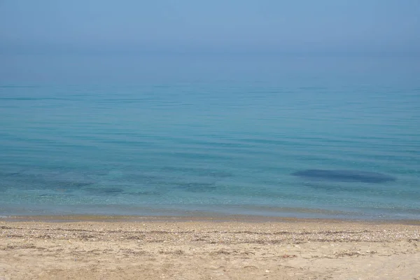 Denizin sakin yüzeyi ve ıssız bir kumsal. Küçük dalgalar ve mavi gökyüzü. Halkidiki, Yunanistan.