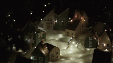 Güzel minyatür. El yapımı dekoratif köy. Noel arifesi. Tatil atmosferi, küçük dekoratif evler, kar ve şehir merkezinde bir Noel ağacı. Kamera sağa doğru hareket ediyor..