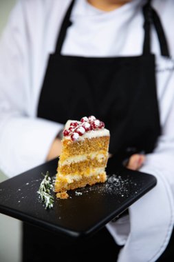 A piece of delicious carrot cake on a black tray in the hands of a skilled chef clipart