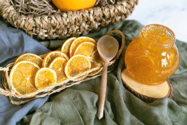 Ahşap bir standa portakal reçeli ve tahta bir kaşık ve kurutulmuş portakalla tekstil. Hasır bir sepetle
