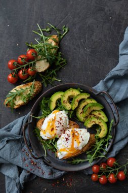  Haşlanmış yumurta, avokado ve roka ile kahvaltı. Tekstil arka planında dökme demir bir tavada servis edilmiş. Üst görünüm