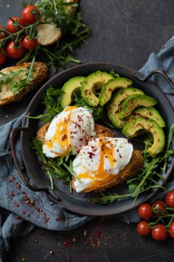  Haşlanmış yumurta, avokado ve roka ile kahvaltı. Tekstil arka planında dökme demir bir tavada servis edilmiş. Üst görünüm