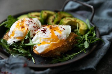  Bir dilim kızarmış ekmek, avokado, roka, vişneli domates ve baharatla nefis ve lezzetli bir kahvaltı. Dökme demir bir tavada servis edilmiş, siyah arka planda tekstil ile servis edilmiş. .
