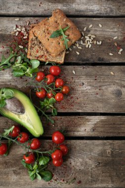  Uzayı kopyala Ahşap bir arka planda, solda, kiraz domatesleri, avokado, sarımsaklı çörek, şifalı otlar ve ayçekirdeği sebzelerle serilir. Sağlıklı beslenmenin kırsal tarzı
