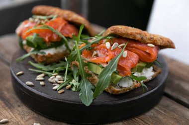 Öğle yemeği için lezzetli bir aperatif. Hafif tuzlu somonlu lezzetli bir sandviç. Yeşillik, arugula yeşilliği ve ayçekirdeği ile! Ahşap bir tabakta ve kırsal bir zeminde servis edilmiş. Yatay yönelim