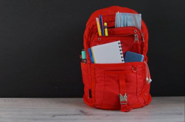 Masa başındaki okul kırtasiyesinde kırmızı sırt çantası var.                               