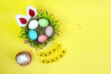 Tavşanla Paskalya tatili geçmişi. Sarı arkaplan küplerinde süslü Paskalya yumurtaları ve pasta. Mutlu Paskalyalar.