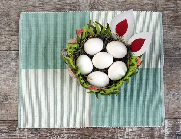 Tahta bir sepetin içinde çim ve tavşan kulakları olan yumurtalar.                               