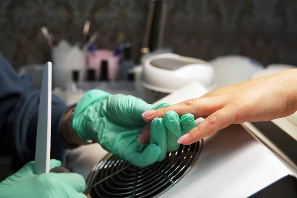 Manikürcü tırnak törpüsü kullanarak pürüzsüz ve temiz bir şekil yaratıyor. Tırnak cilası sürmeye hazırlanan kadın elinin yakın çekimi. Güzellik uzmanı tırnak törpüsü ile tırnak törpülüyor. Profesyonel tırnak bakım servisi..                               