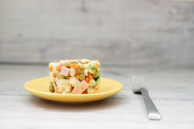 Sarı tabakta bezelye filizleriyle süslenmiş Olivier salatası..