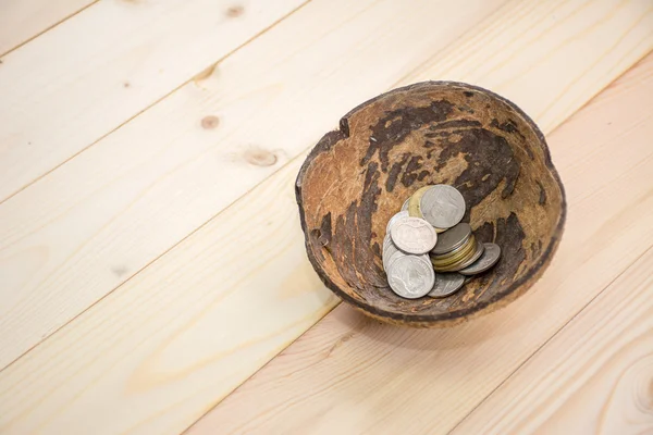 Monedas en cáscara de coco en el suelo de madera, uso para el concepto de mendigo — Foto de Stock