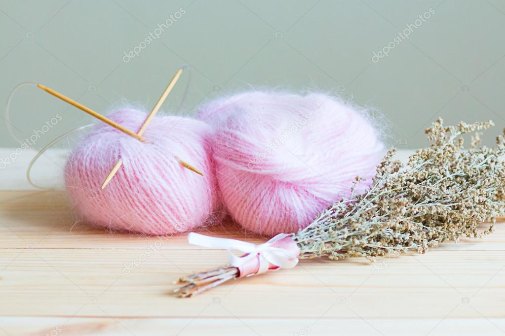 two skeins of pink yarn with knitting needles on a wooden background with a beam of near Artemisia
