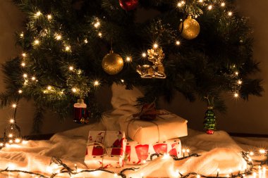 Noel hediyelerini dekore edilmiş gerlyandoy, parlak sarı ve kırmızı topları Noel ağacı altında